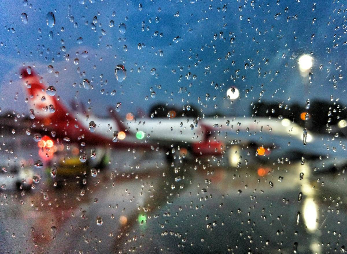 Traveler checking flight status on phone during storm with weather related itinerary change notice displayed